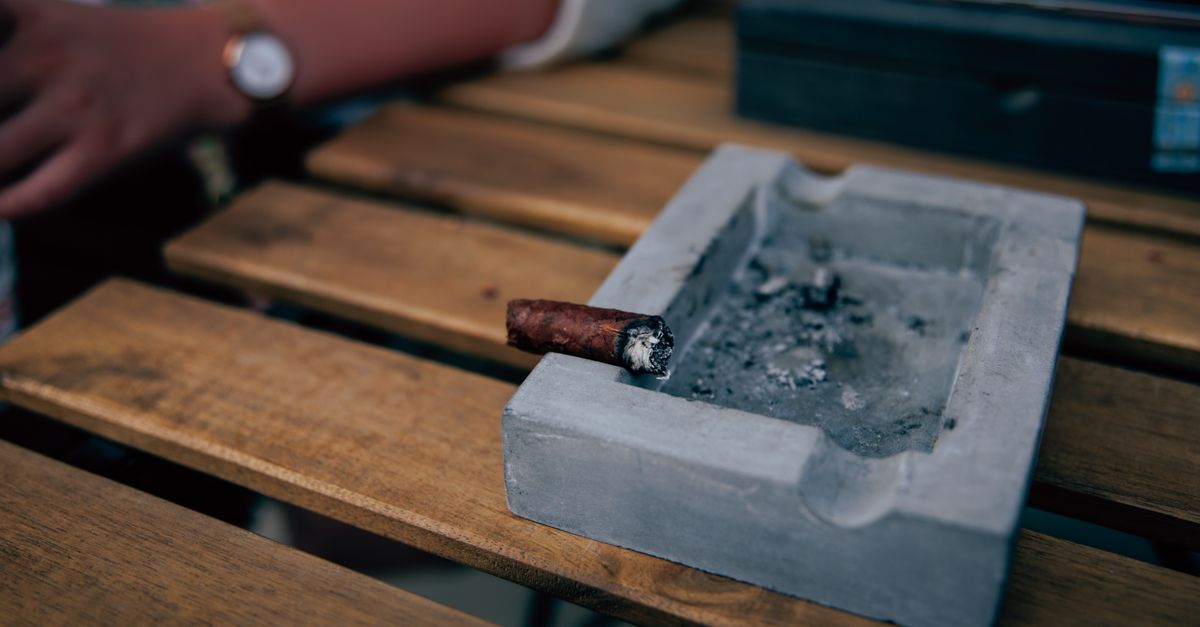 A close-up shot of a concrete ashtray with a burning cigar on a wooden table.