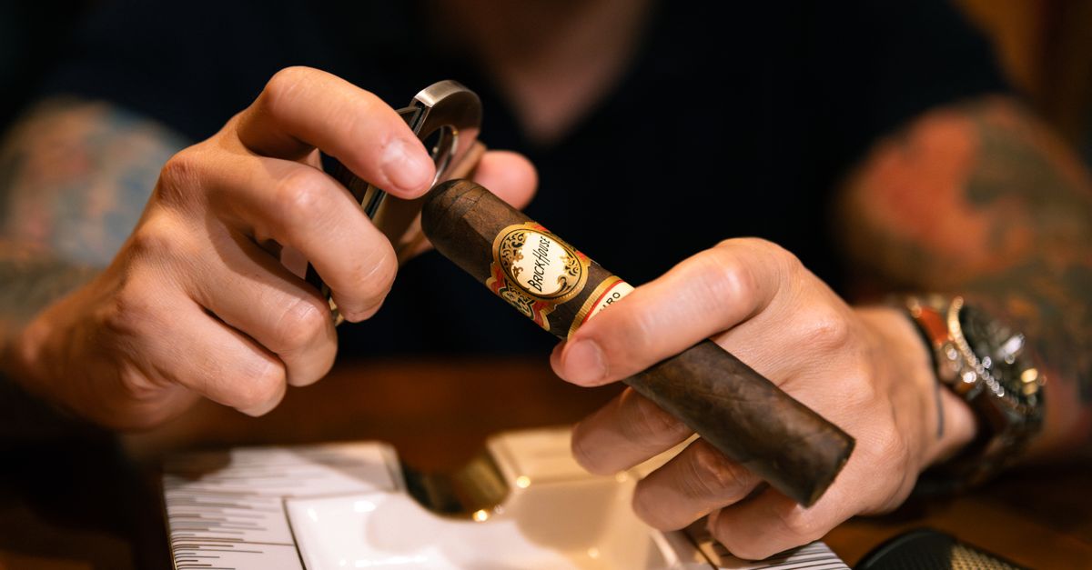 A detailed close-up of a man carefully cutting a cigar, showcasing precision and craftsmanship.