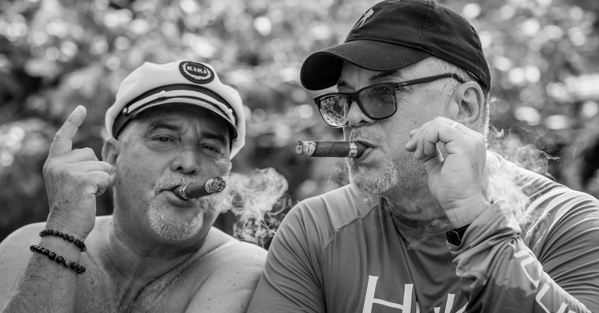 Two middle-aged men smoking cigars outdoors in Miami, captured in a candid black and white shot.