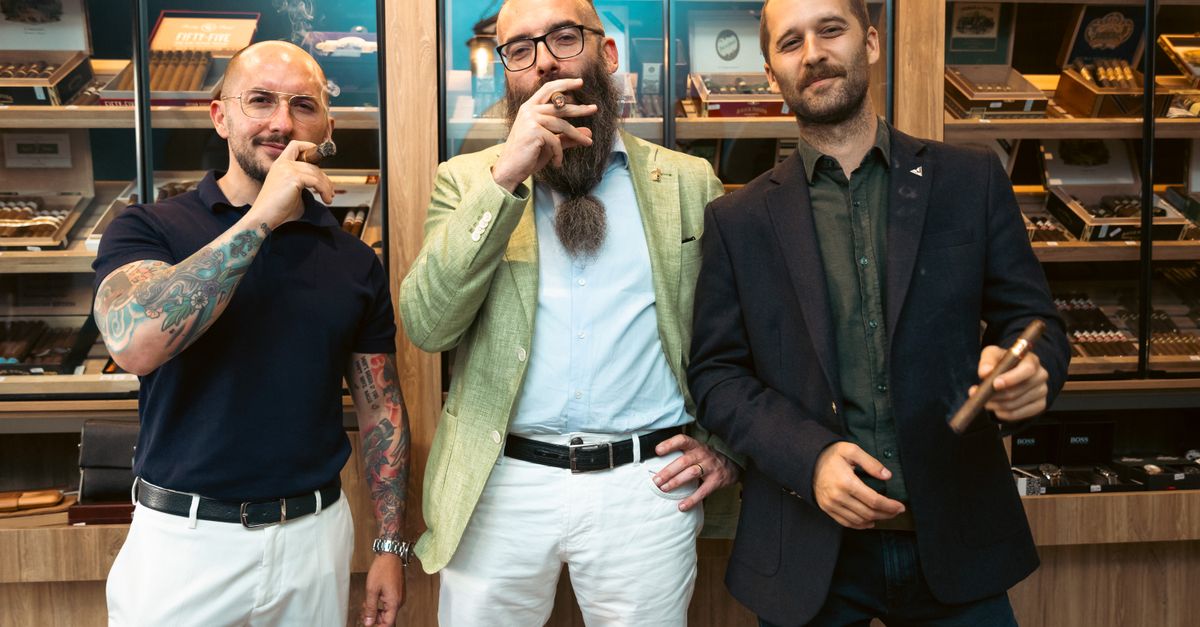 Three stylish men with tattoos pose confidently with cigars in a cigar store.