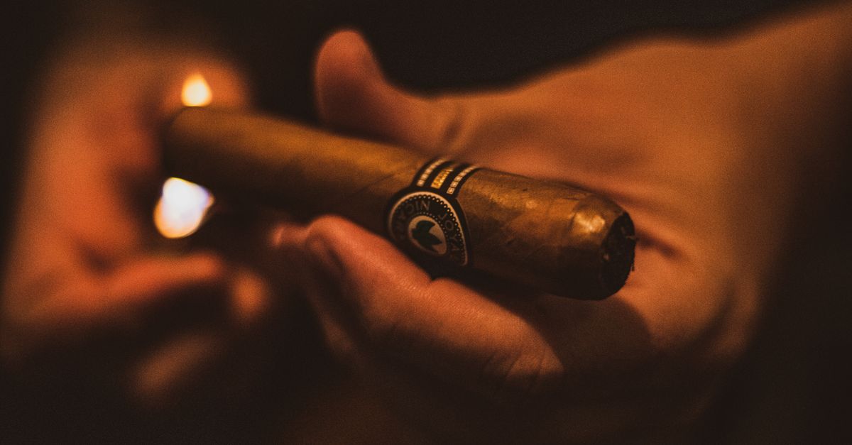 A detailed close-up shot of a hand lighting a cigar in a dark setting.