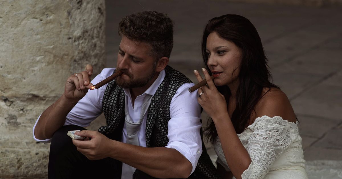 A couple enjoying cigars while seated outdoors in wedding attire, capturing a candid moment.