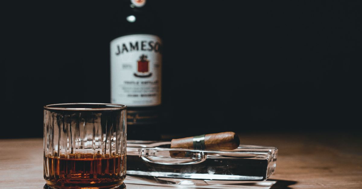 Elegant scene of whiskey glass and cigar on a wooden table with a bottle in the background.