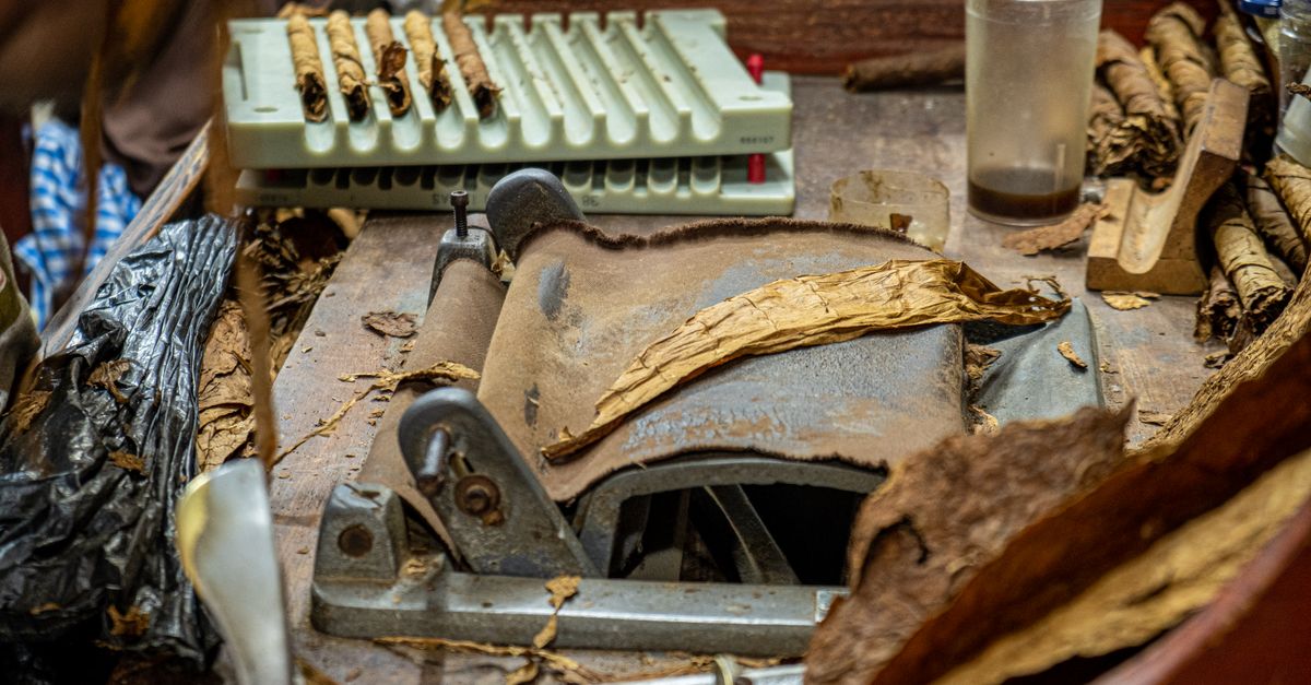 Close-up of a vintage tobacco rolling machine and cigars in a rustic workspace.