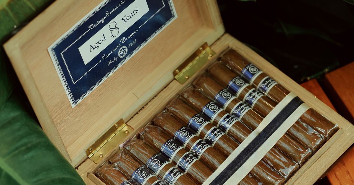 Open box displaying a collection of luxury vintage cigars nestled among green foliage.