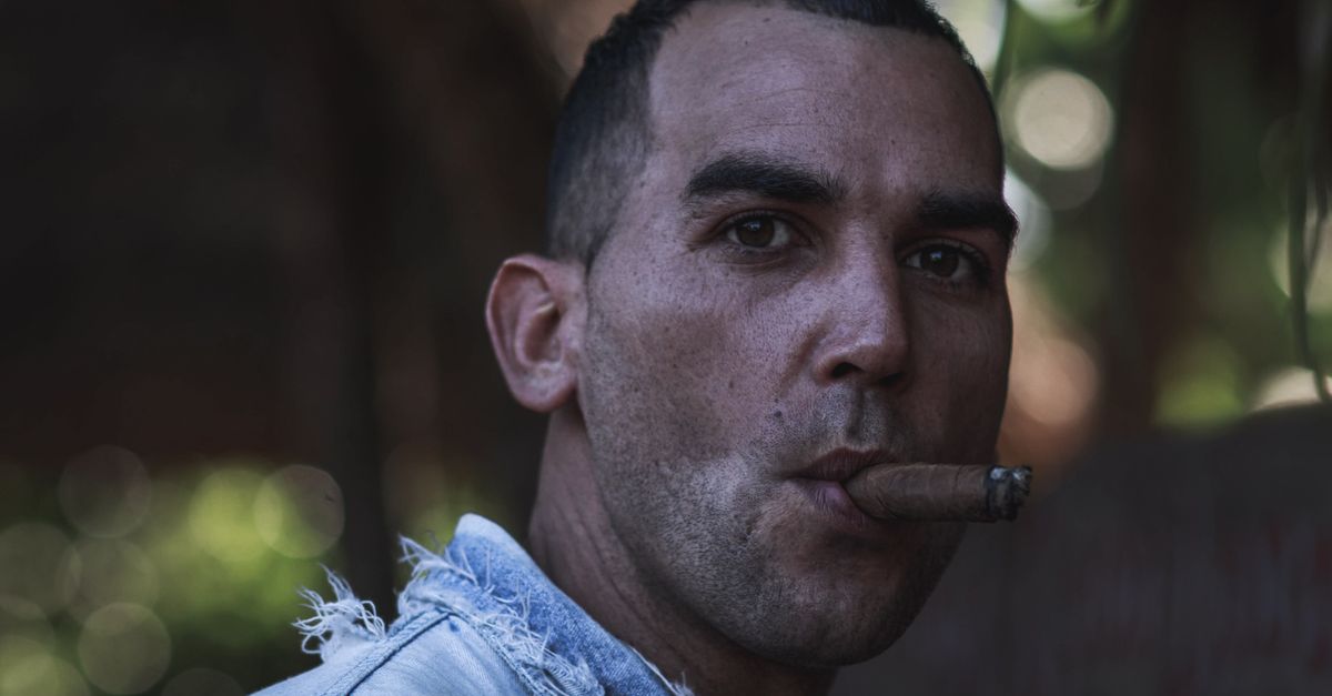 Portrait of a man smoking a cigar with a blurred natural background.
