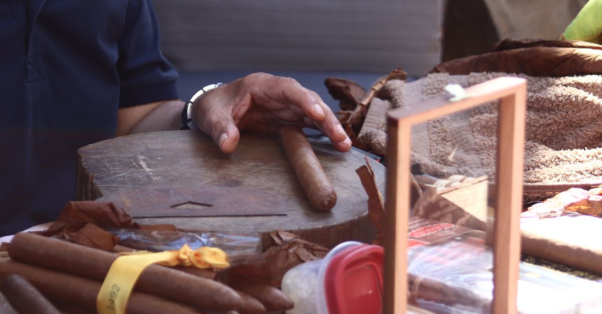Detailed view of cigar crafting with a hand positioned on a table, depicting the art and tradition of cigar making.