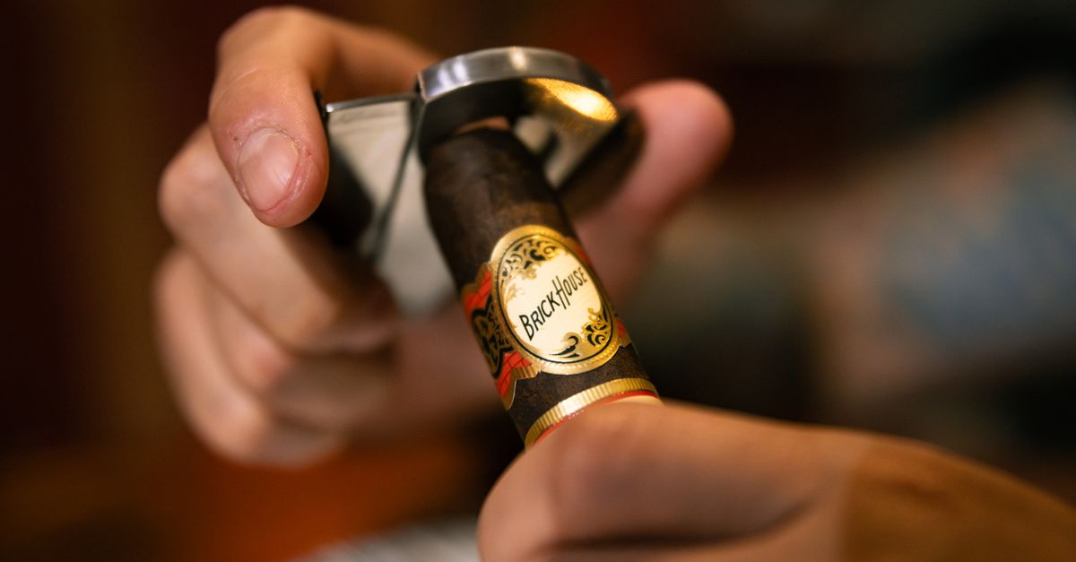 Focused image of a person using a cigar cutter on a premium cigar indoors.